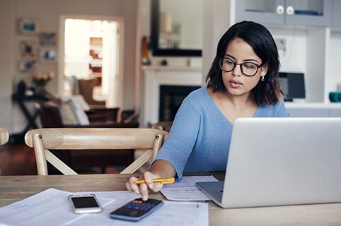mujer joven usando una calculadora y trabajando en su computadora portátil