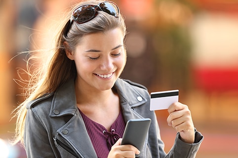 adolescente sonriendo y usando su teléfono para pagar una compra de tarjeta de crédito como usuario autorizado en la tarjeta de un padre