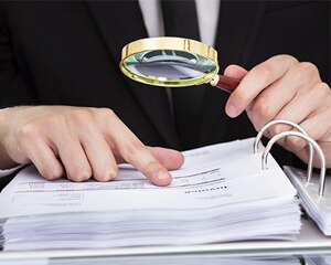 Person with magnifying glass looking at papers in a binder