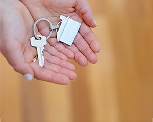 two hands holding keys with a keychain in the shape of a house