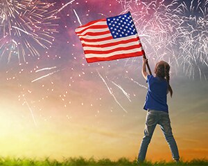 little girl waving an American flag against a backdrop of fireworks