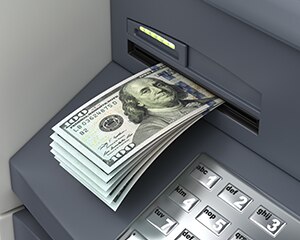 Pila de billetes de cien dólares que salen de un cajero automático