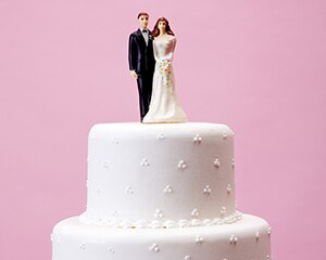 wedding cake with bride and groom topper, pink background