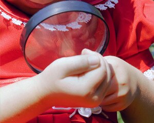 Child looks at her hands through magnifying glass