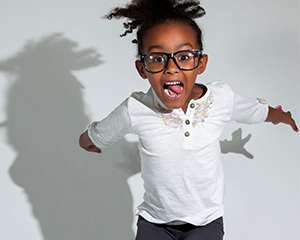 A tittle girl jumping, laughing, and casting shadow on wall