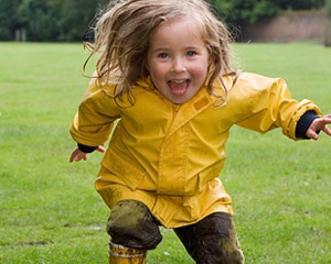 Foto de una niña pequeña corriendo bajo la lluvia con un impermeable