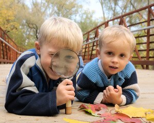 Hermanos pequeños mirando las hojas caídas a través de una lupa