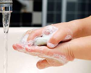 Close-up photo of a child's hands lathered in soap and rinsing in a sink