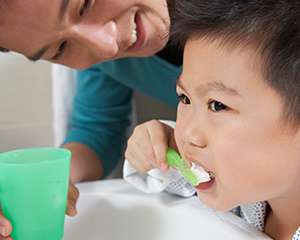 Foto de una niña joven cepillándose los dientes mientras su madre ayuda