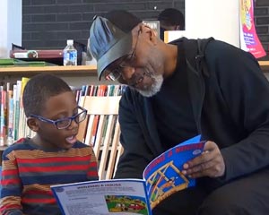 hombre con gorra lee un libro a un niño en un ambiente de aula.