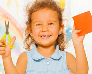 Little girl smiling while using scissors and construction paper