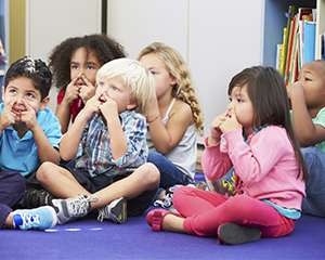 Photo of a group of children sitting on the floor holding their noses