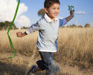 Young boy runs in a field while flying a kite