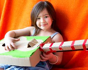 A little girl playing a guitar made of recycled materials