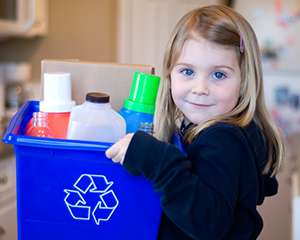 Photo of a little girl carrying a full recycling bin and smiling
