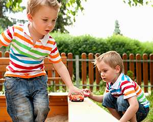 Niños gemelos rodando automóviles de juguete sobre una viga de madera