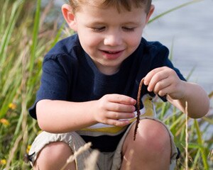 Niño joven juega con un gusano en una zona de césped cerca del lago