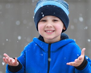 Niño joven con las manos extendidas para sentir la nieve cayendo