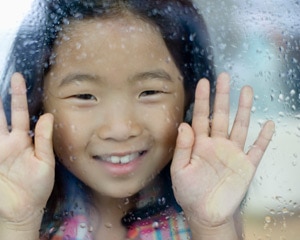 Young girl looking at rain through window