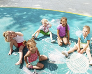  Group of young children playing outside with sidewalk chalk