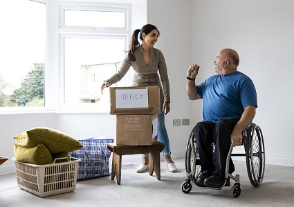 Man using wheelchair speaking to woman with moving boxes.