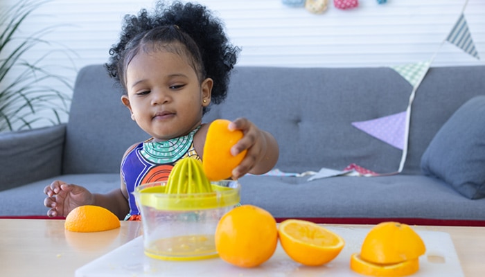 Female toddler making orange juice with a juicer