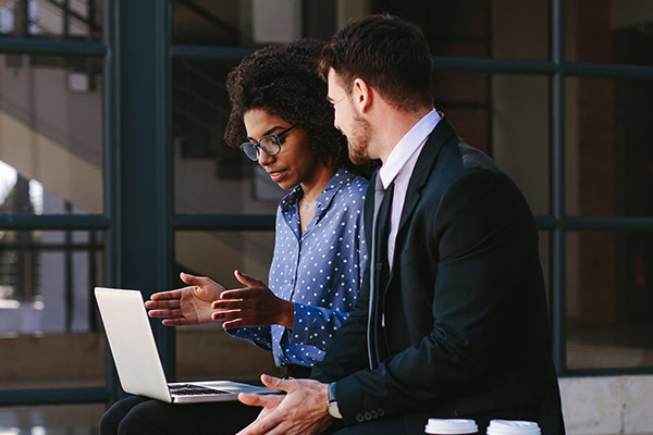 A woman and a man both in business attire discussing something they are viewing on a laptop.