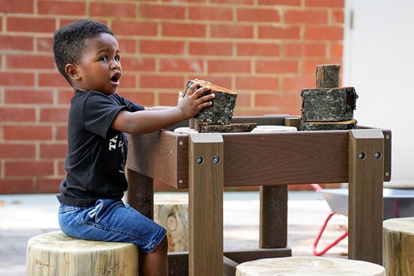 Nature based play and learning space in Charlotte with a child enjoying log blocks.