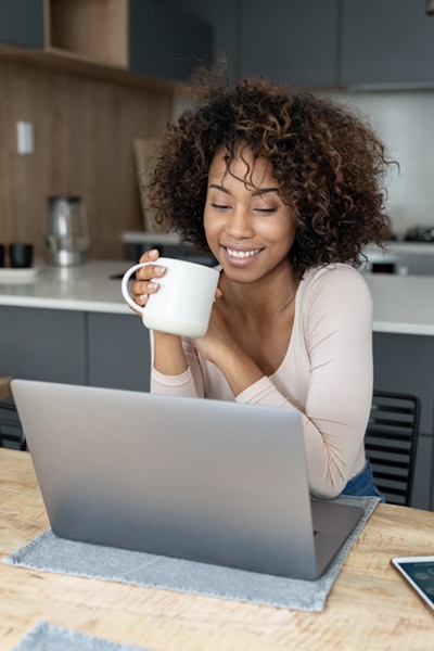 A smiling woman drinking coffee looking at her computer screen